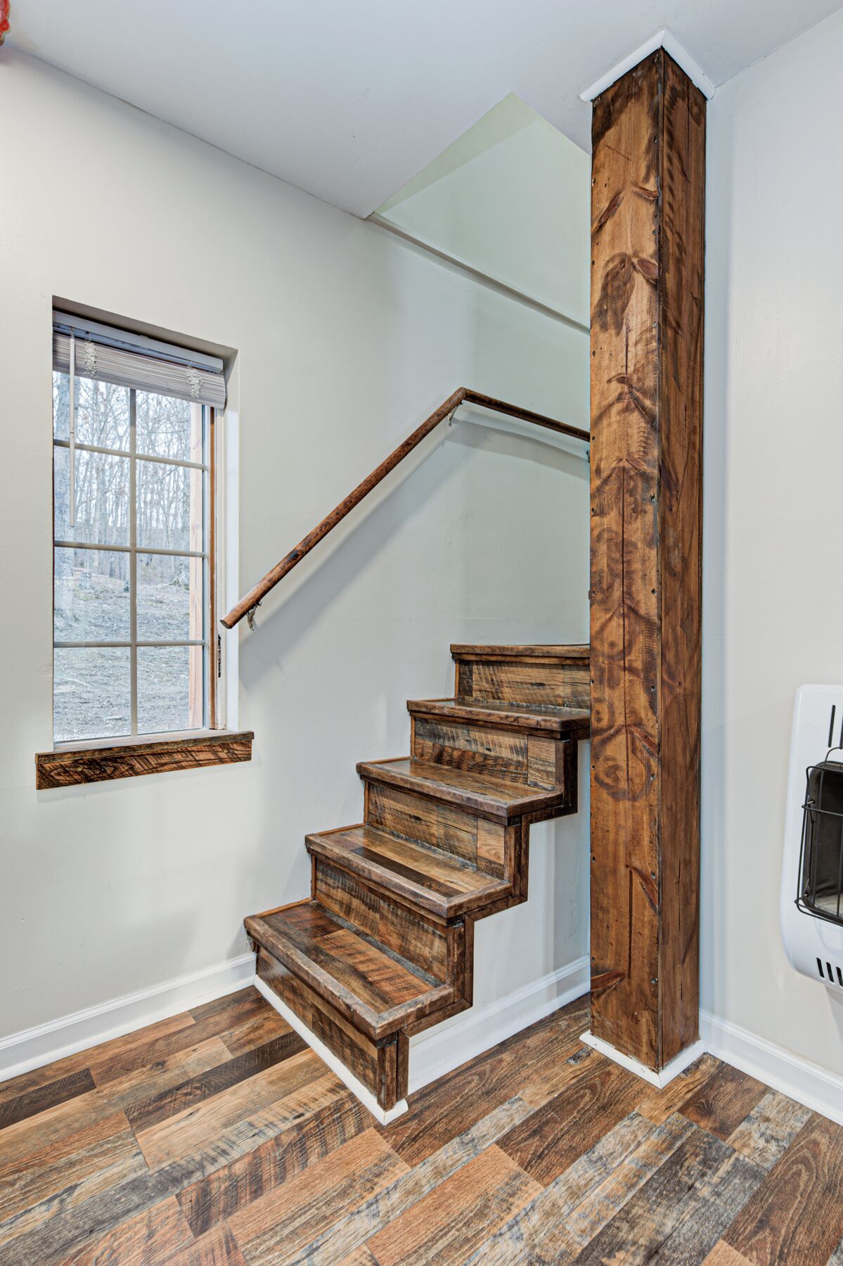 A wooden staircase with a glass balustrade, a window with blinds, and a wall-mounted air conditioning unit.