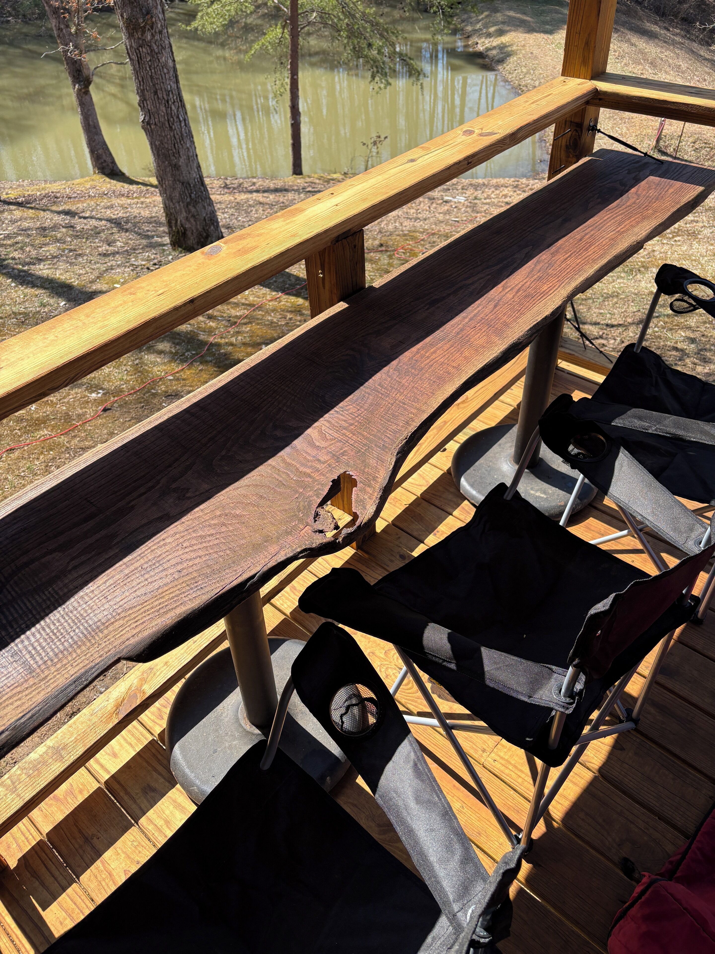 A wooden deck with a bench and two folding chairs.