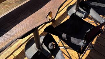 A wooden deck with a bench and two folding chairs.