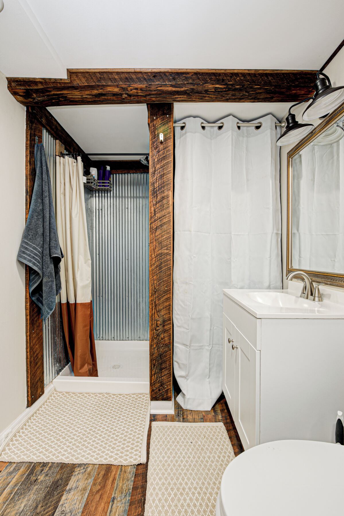 Un baño con techo de vigas de madera, un lavabo blanco, un espejo y una zona de ducha con cortina.