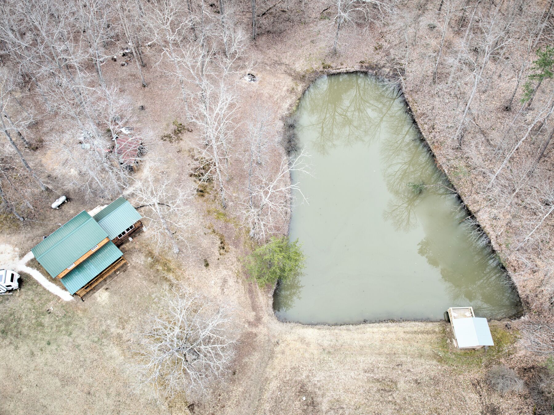 An aerial view of a property with a pond, a small building with a green roof, and a white trailer.