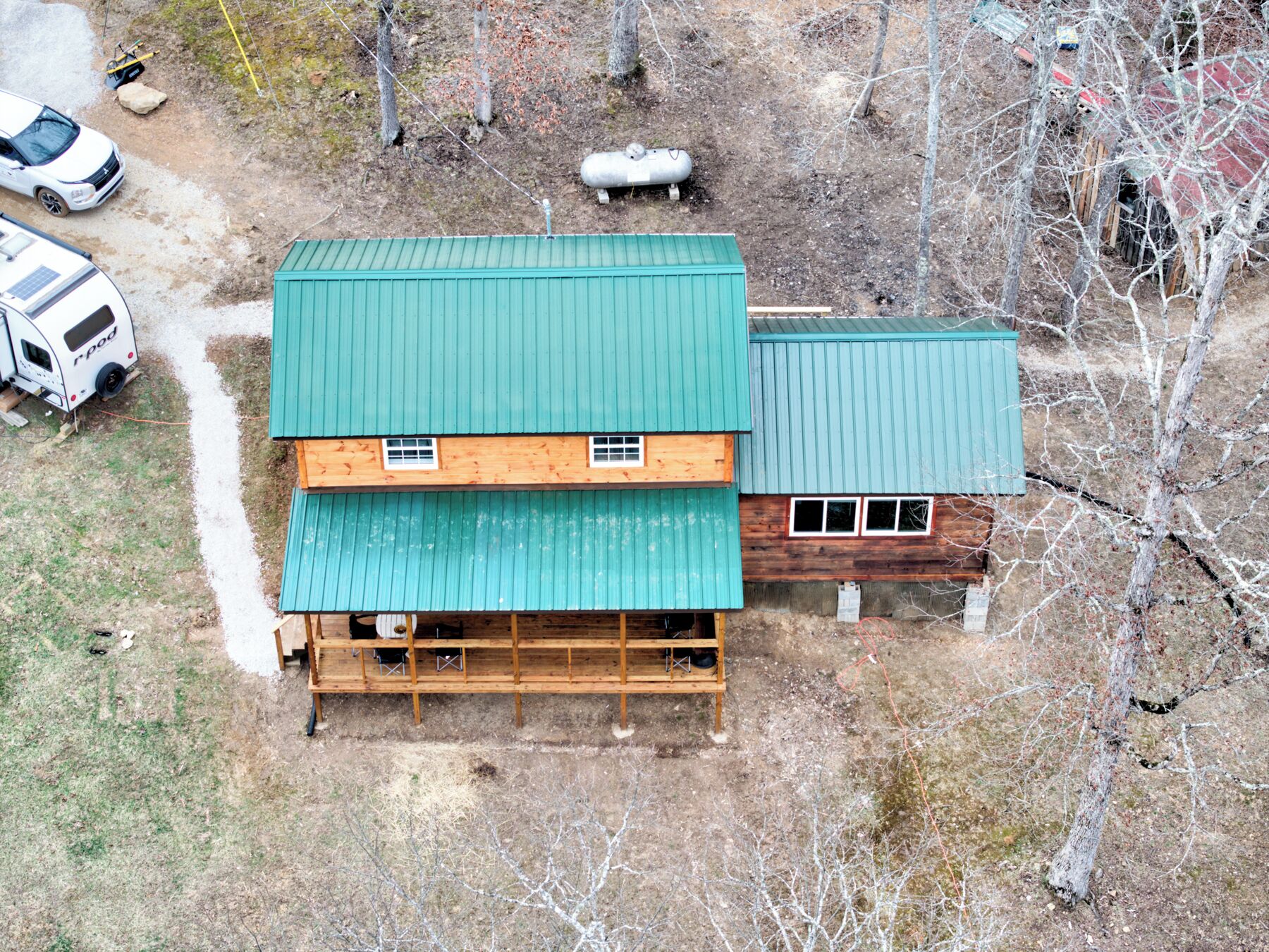 Une cabane à deux étages, avec un toit en métal vert, une terrasse en bois et un petit abri attenant.