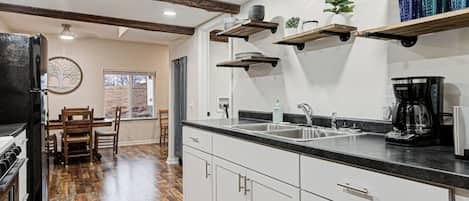 A kitchen with white cabinets, a black countertop, and a coffee maker. There are wooden beams on the ceiling and a window with a view of the outdoors.