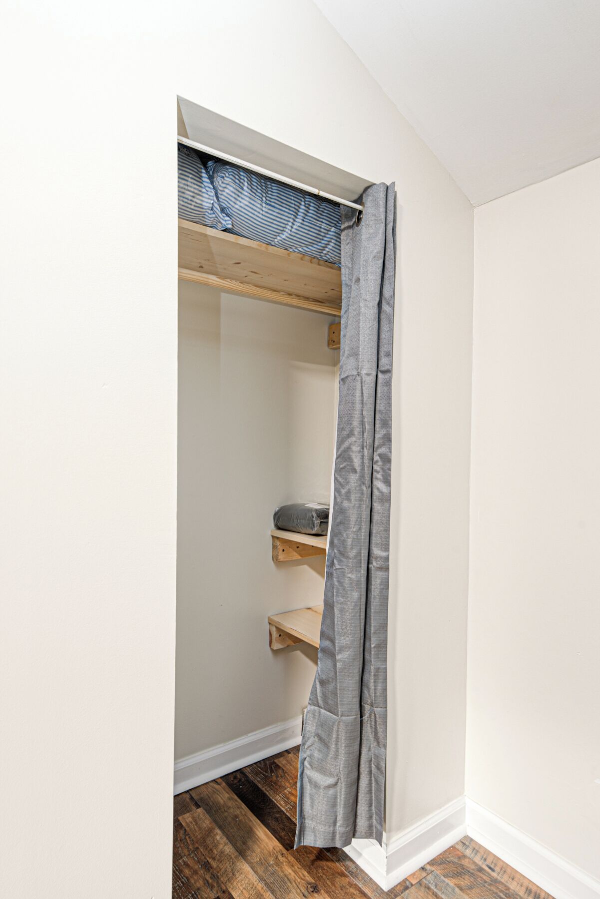 Un couloir étroit dans lequel se trouve une étagère en bois contenant une couverture pliée et un oreiller.