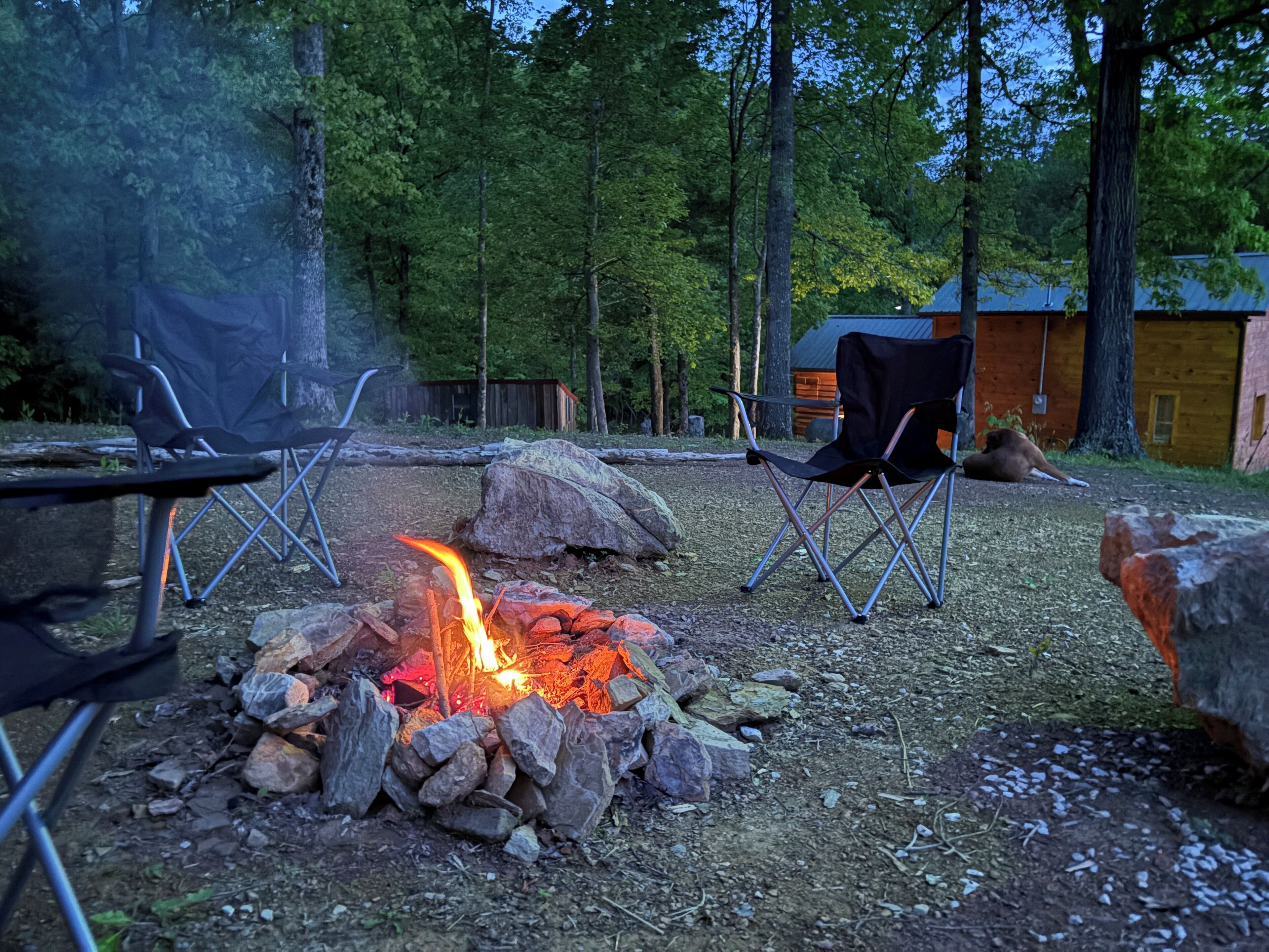 A campfire surrounded by rocks and two folding chairs.