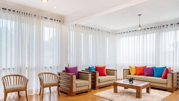 Een moderne woonkamer met houten meubels, waaronder twee fauteuils en een bank met kleurrijke kussens.