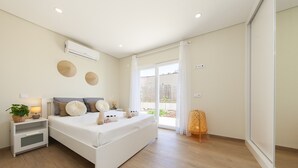 A modern bedroom with a large bed, bedside tables, and a view of the outdoors through a sliding glass door. - Peaceful villa w/ pool, BBQ & ping-pong table (Alcantarilha)