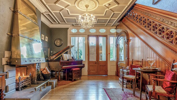 Een statige kamer met een vleugelpiano, een open haard en een trap met versierde houtsnijwerken.