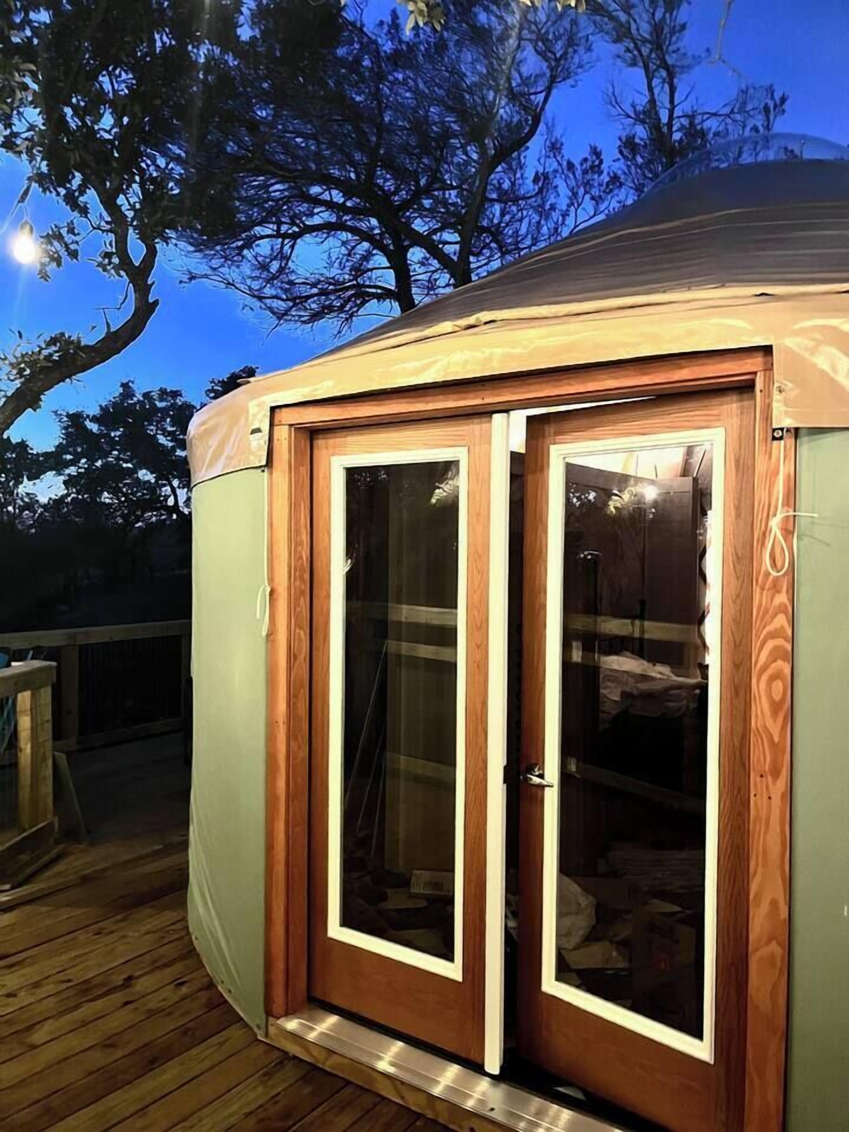 A wooden structure with two glass doors, a deck, and a tree in the background.