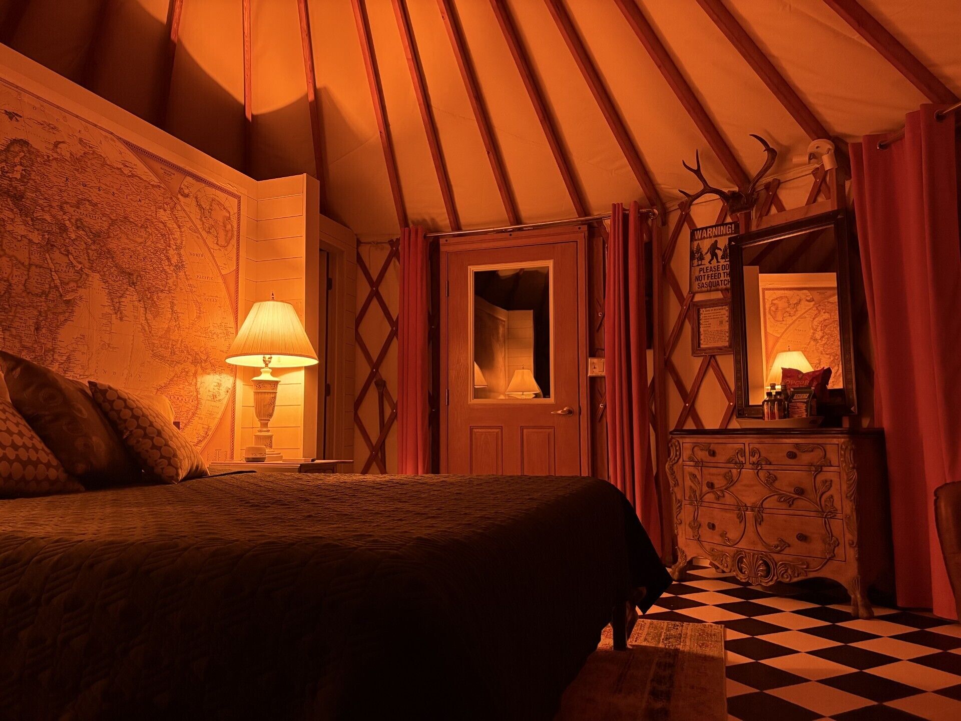Een kamer met een bed, een lamp, een dressoir, een spiegel en een kaart aan de muur.