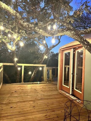 A wooden deck with string lights, a glass door, and a metal chair. - Stargazer Yurt - Secluded Texas Glamping (Gatesville)
