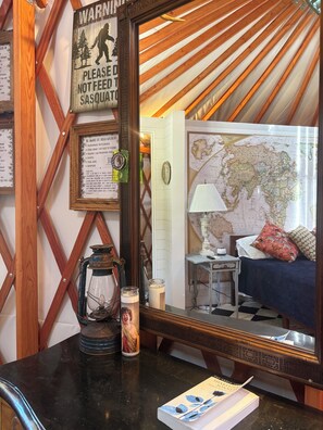 Habitación con un espejo grande que refleja una cama, un mapa y una lámpara. Una pared de madera con un letrero de advertencia y un aviso enmarcado sobre fauna.