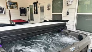A hot tub with a wooden deck, surrounded by a white exterior wall with windows and a door. - Atlanta Game House with Hot Tub (Riverdale)