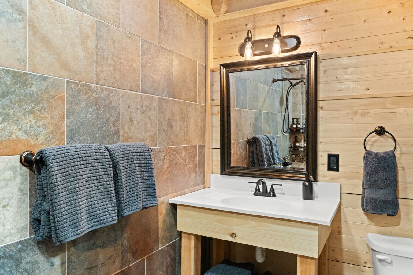 A bathroom with a wooden wall, a tiled floor, a sink with a mirror, and two towels hanging on towel rings.