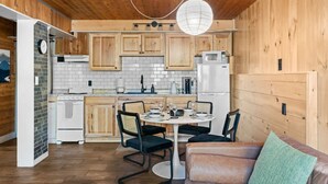 A compact kitchen with wooden cabinets, a white refrigerator, and a dining area with a round table and chairs. - Cabin on Mtn, Seasonal Pool Access w Panoramic Views! Hike, Golf, Swim, Unwind! (Lanesville)