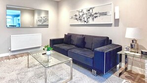 A modern living room with a sofa, a glass coffee table, a large abstract painting, a radiator, and a television mounted on the wall. - Charming 2-bedroom apartment with WiFi in London (London)