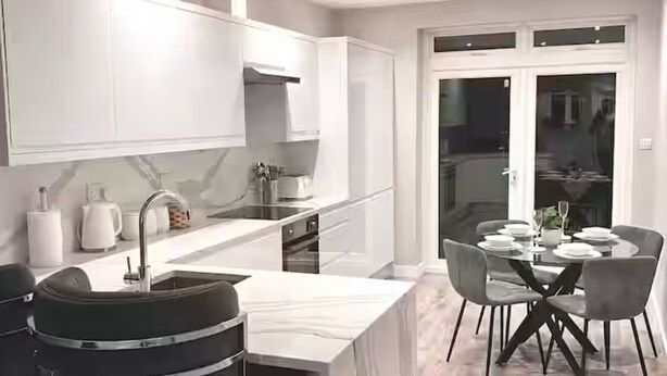 A modern kitchen with white cabinets, a marble countertop, and a dining area with a round table and chairs. - Charming 2-bedroom apartment with WiFi in London (London)