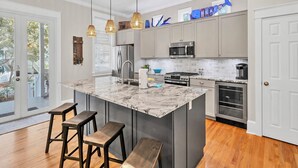 A modern kitchen with a central island, stainless steel appliances, and a view to the outside. - New List-4BR all en-suite steps to deeded beach and 2 community ‘1 heated’ pools (Santa Rosa Beach)