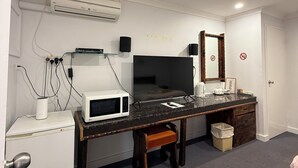 Egy kis méretű szállodai szoba, amelyben található egy kis konyhasarok, egy síkképernyős televízió, egy fa íróasztal és egy kis szemeteskosár.