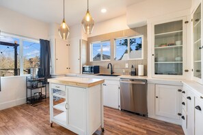 Une cuisine moderne avec des meubles blancs, un îlot central en bois et des luminaires suspendus.