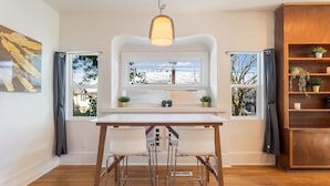 A modern kitchen with a white table, two bar stools, a pendant light, and a window with a view of a snowy landscape.