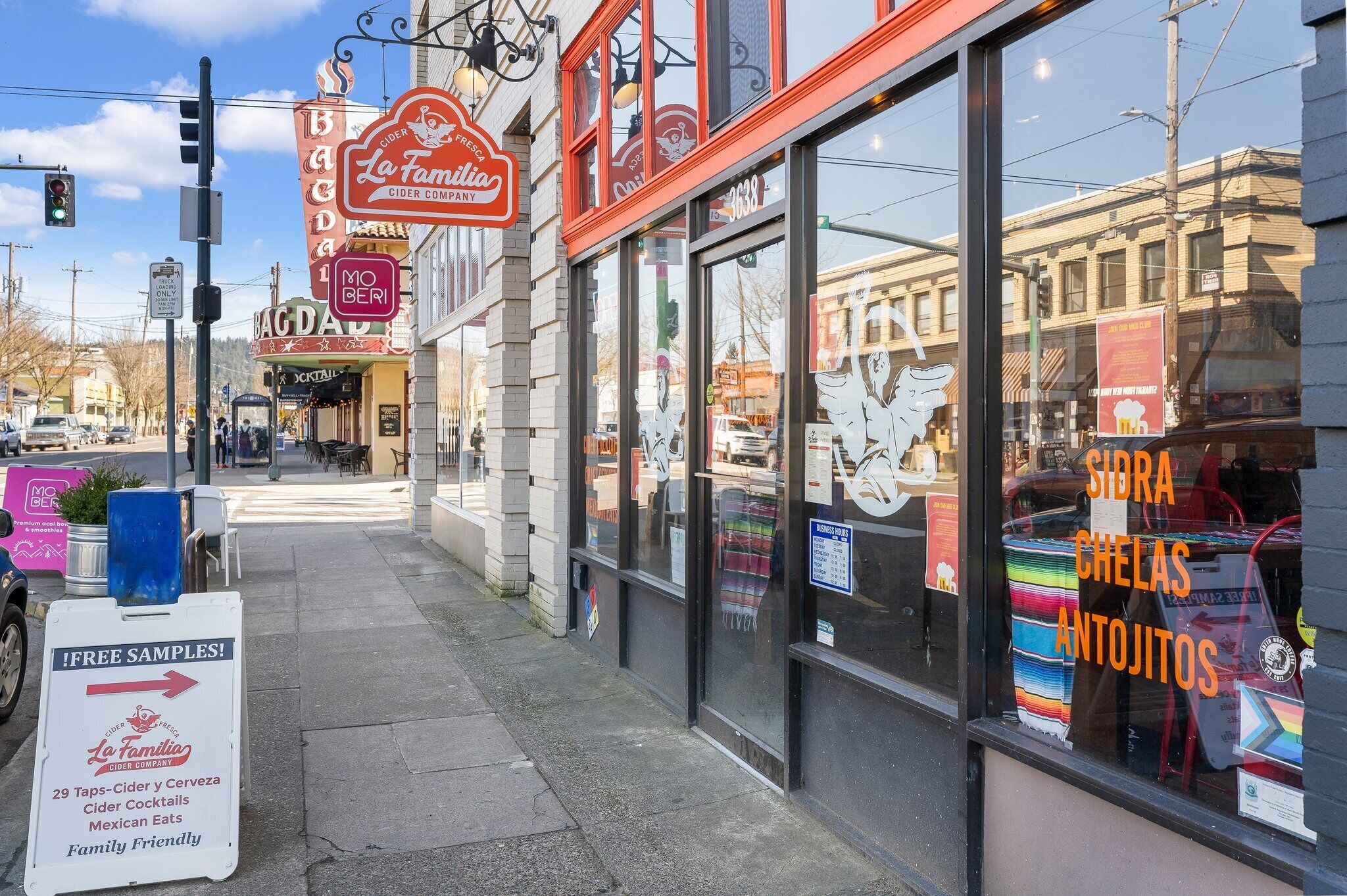 A storefront with a sign for La Familia Cider Company, offering free samples and a variety of drinks.