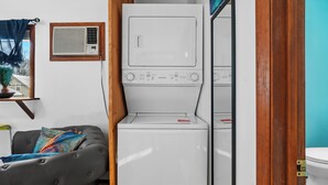 A laundry area with a washing machine and dryer, a window with blinds, a chair, and a small table with a plant. - Charming 3-bedroom duplex with study space, WiFi in cool  Scituate. (Scituate)