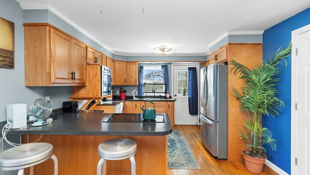 A kitchen with wooden cabinets, a stainless steel refrigerator, a built-in oven, a sink, and a window with curtains. - Charming 3-bedroom duplex with study space, WiFi in cool  Scituate. (Scituate)