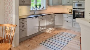 A kitchen with white cabinets, a window with plants, a built-in oven, and a striped rug. - 3 bedroom stunning home in Tingsryd (Tingsryd)