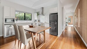 Una cocina moderna con armarios blancos, un refrigerador de acero inoxidable y una mesa de comedor de madera con sillas.