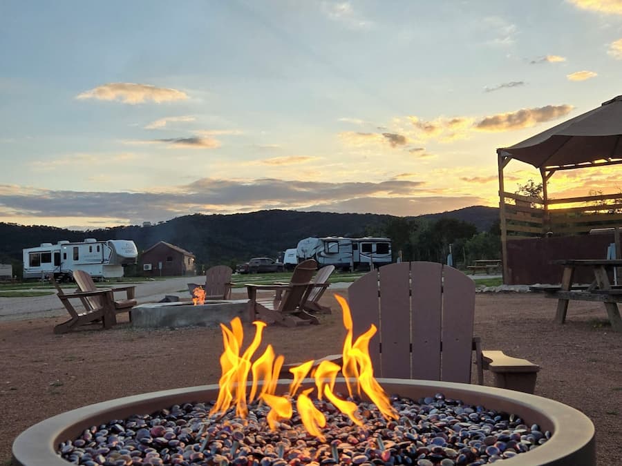 Una fogata con llamas, rodeada de asientos exteriores y vehículos recreativos en un camping.