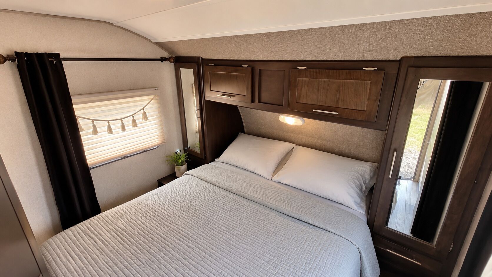 A bedroom with a bed, curtains, a window, and a plant.