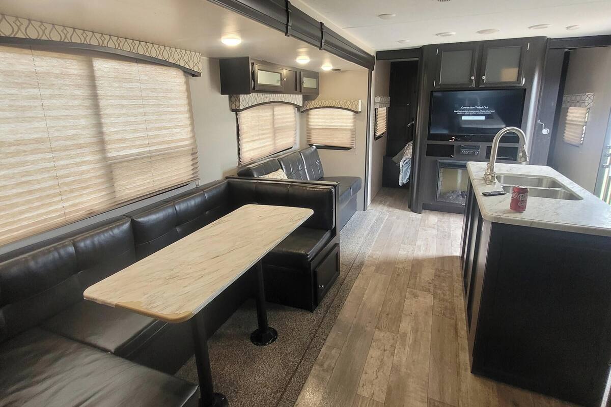 Interior compacto de una autocaravana con kitchenette, comedor con mesa y bancos, y zona de estar con sofá.