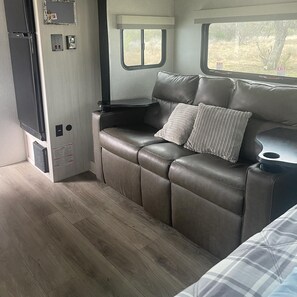 A compact RV interior with a sofa bed, a small table, and a window.