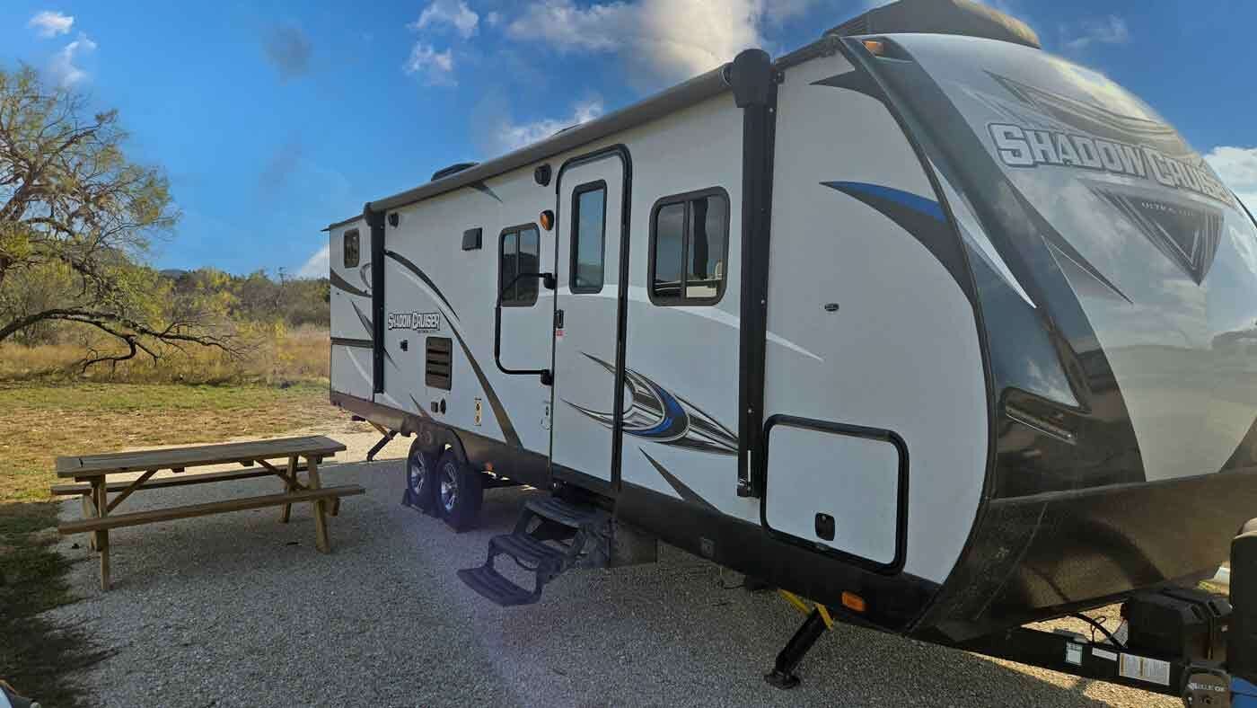 Una caravana con puerta corredera, un banco y una mesa de picnic.