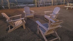Tres sillas Adirondack dispuestas sobre un suelo de grava con luces colgantes.