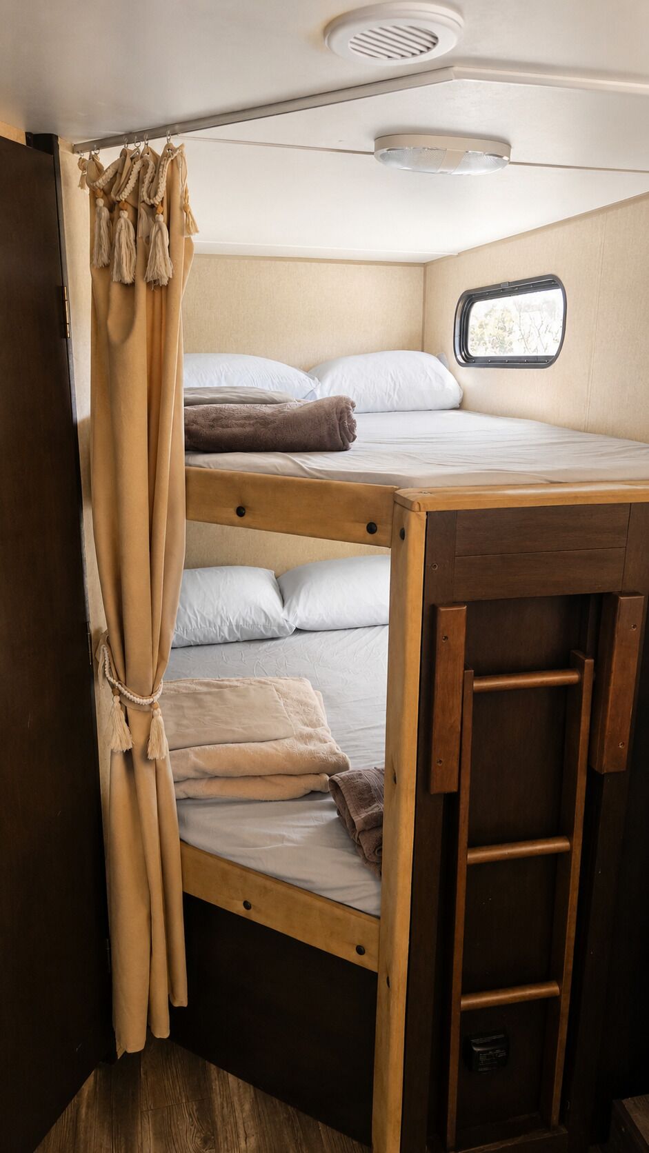 A bunk bed with a ladder, a window with a view, and a curtain.