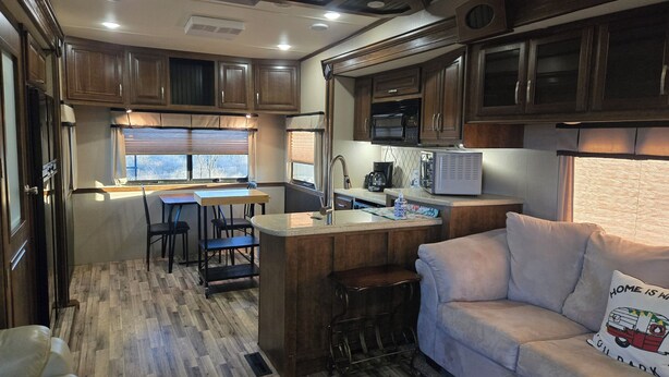 Cocina compacta para autocaravana con armarios de madera, zona de comedor con mesa y sillas, y una kitchenette equipada con refrigerador y cafetera.