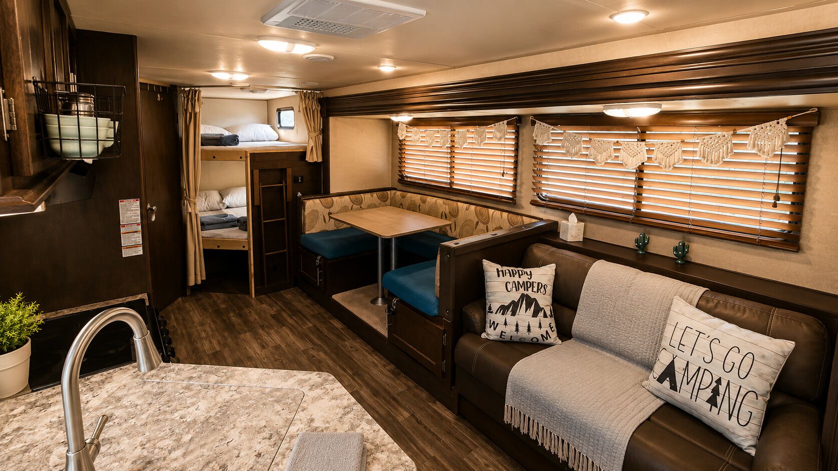 Un intérieur de camping-car compact comprenant un coin cuisine, un espace repas, un coin salon avec un canapé et des coussins, ainsi qu’une petite fenêtre avec des stores.