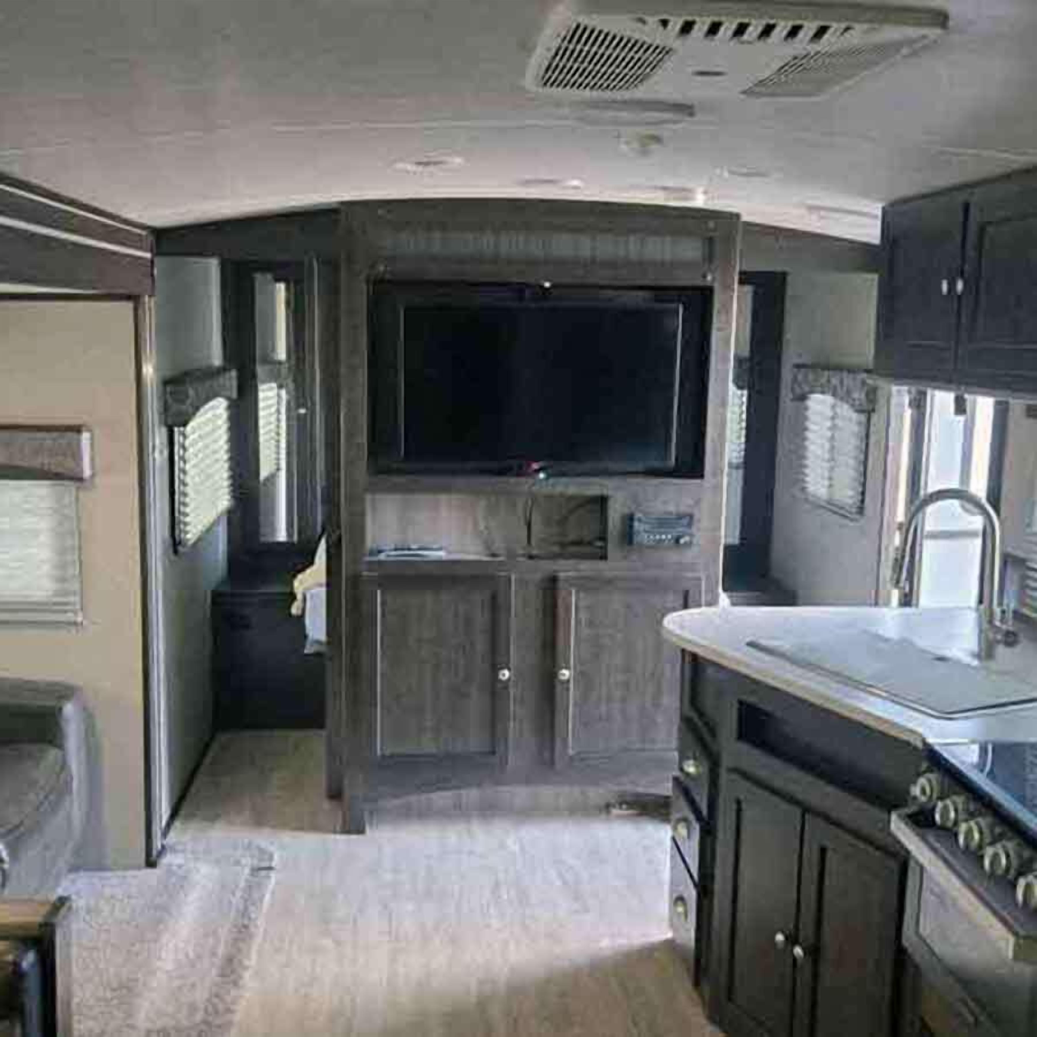 A compact kitchen with a built-in stove, a sink, and a flat-screen TV mounted above the counter.