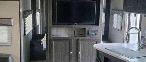 A compact kitchen with a built-in stove, a sink, and a flat-screen TV mounted above the counter.