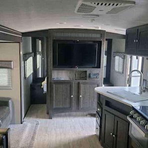 A compact kitchen with a built-in stove, a sink, and a flat-screen TV mounted above the counter.