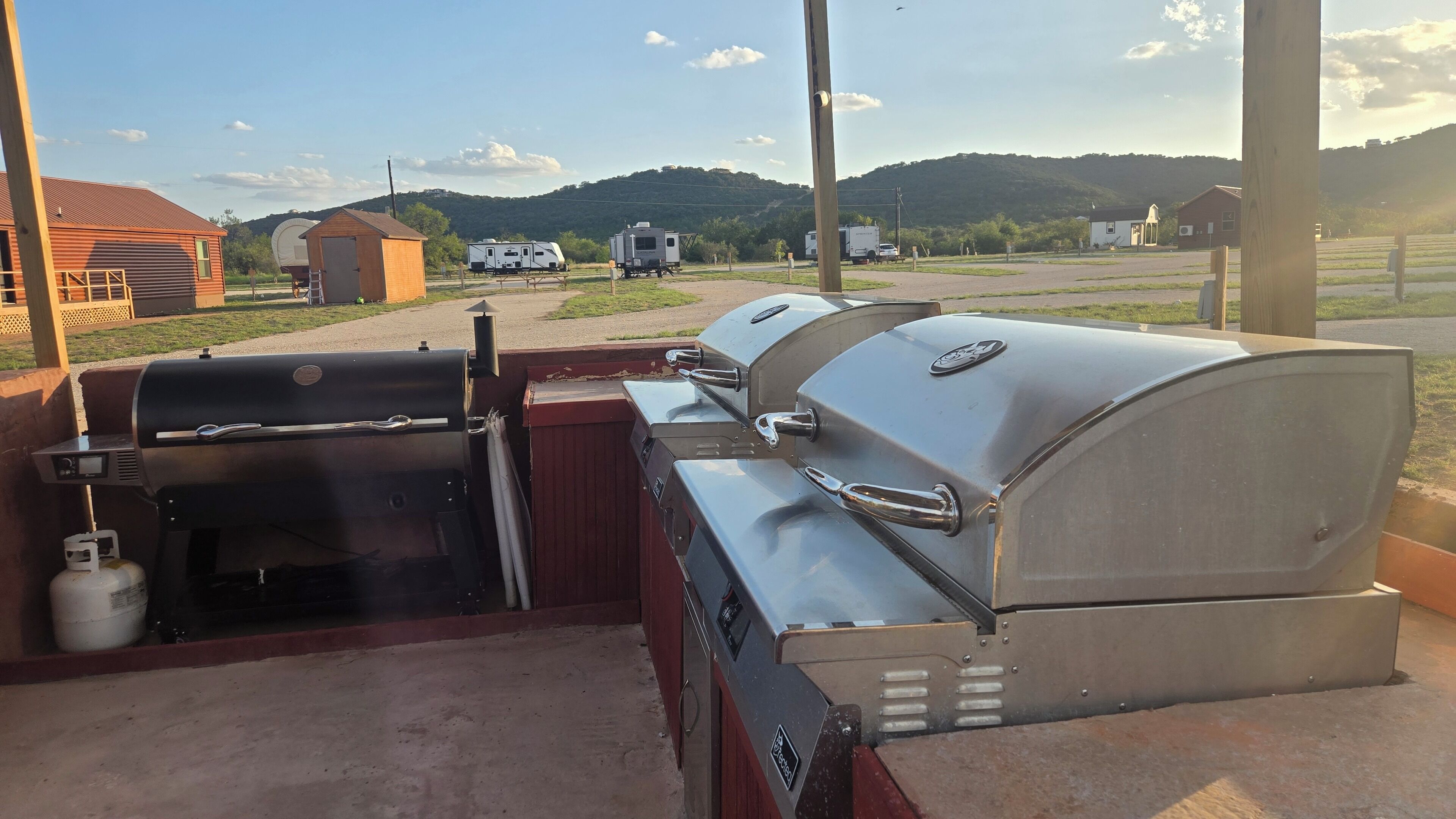 Un barbecue doté d’un panneau de commande numérique et d’une bouteille de gaz, placé sur fond de paysage rural avec des collines et un ciel dégagé.
