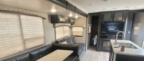 A compact RV interior with a seating area, a kitchenette, and a television.