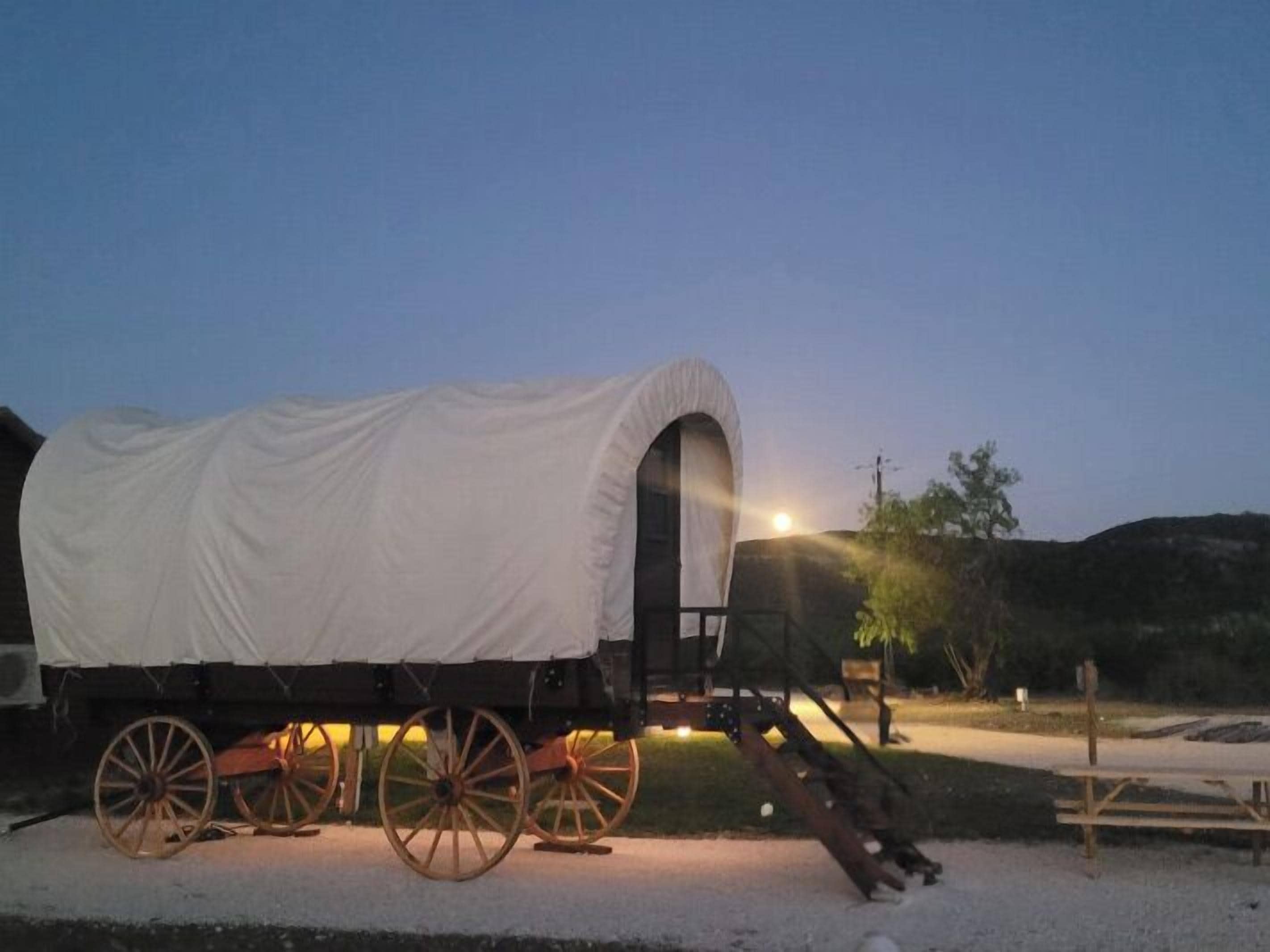 A covered wagon with a white canvas roof parked on a gravel surface.