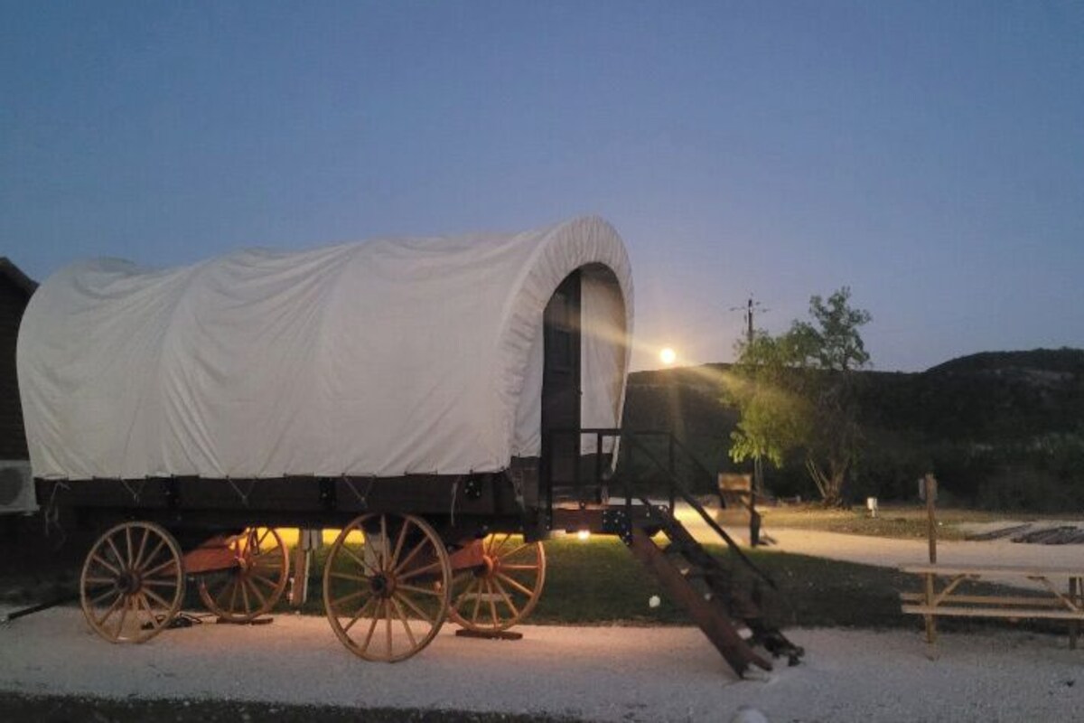 A covered wagon with a white canvas roof parked on a gravel surface.
