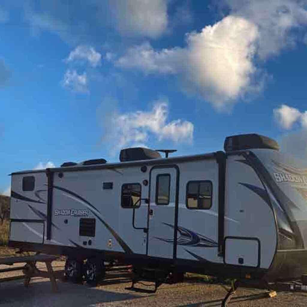Una caravana blanca con la marca "SHADOW CRUISER", una puerta corredera y una ventana pequeña.