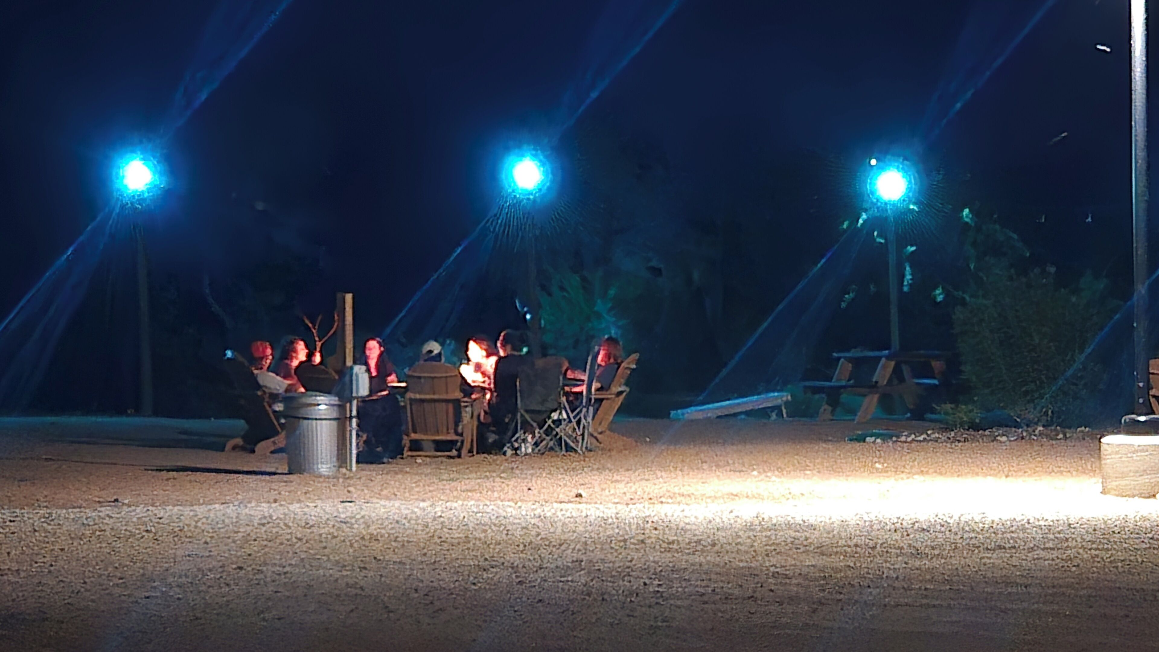 An outdoor dining area with tables and chairs, illuminated by overhead lights.