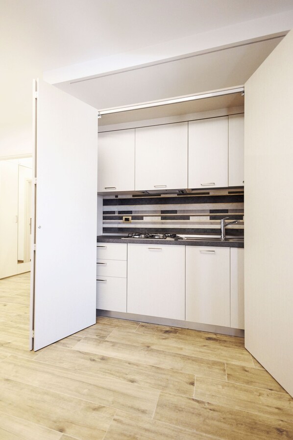 A compact kitchen with white cabinets, a black countertop, and a stainless steel sink.