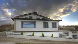 Une maison moderne à deux étages, dotée d’une grande fenêtre, d’un balcon et d’un petit jardin.